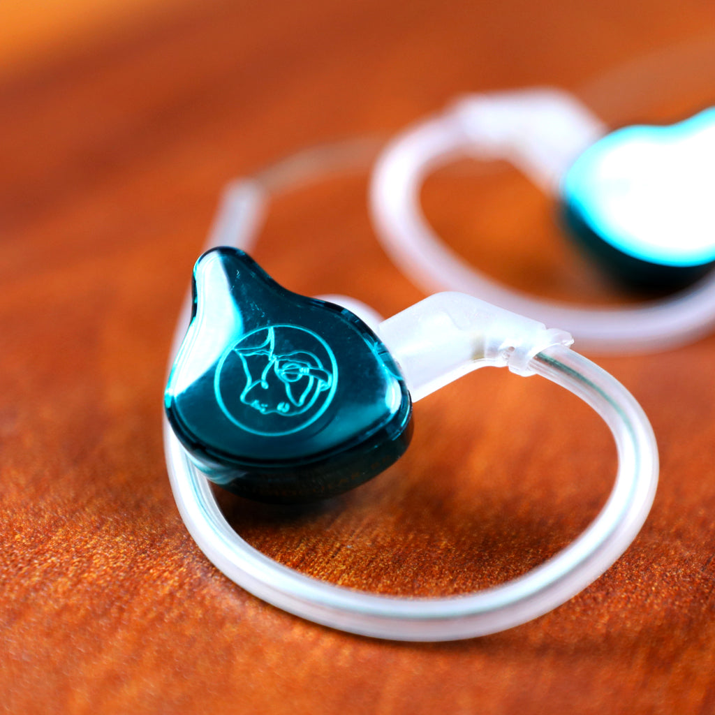 AUDIOCULAR BR 10mm IEM resting on wooden surface, featuring sleek teal finish and transparent over-ear cable for secure fit.
