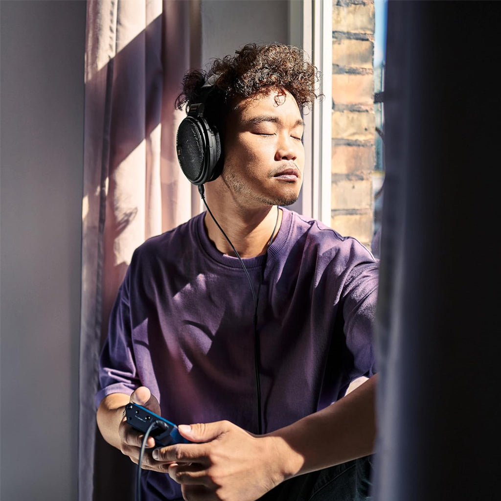 Man relaxing by the window wearing HD 660S2 headphones, enjoying high-fidelity wired audio with deep bass and clarity.