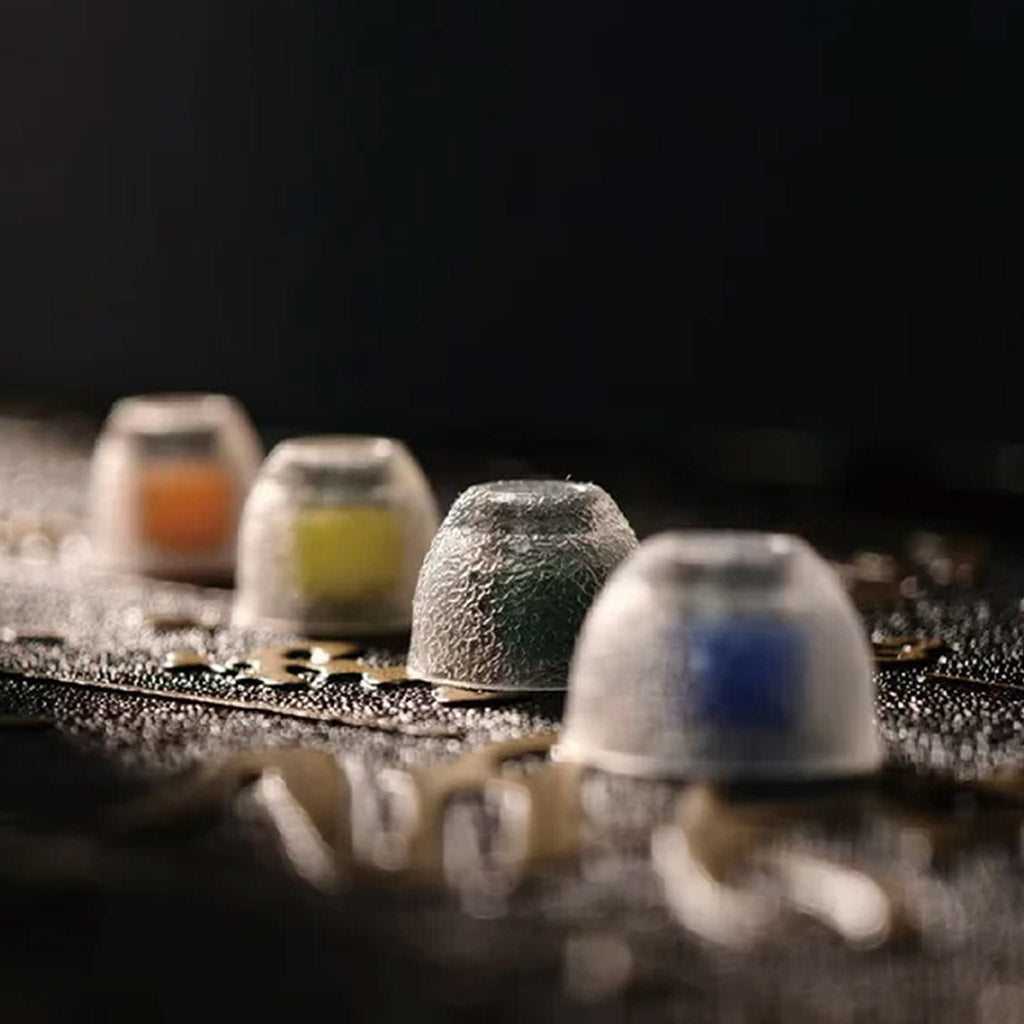 Macro shot of TANGZU Tang Sancai Eartips in different colors on a textured surface, showcasing silicone texture and build.