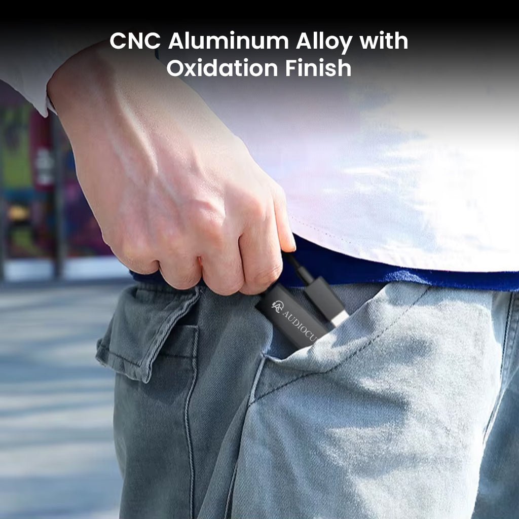 User placing AUDIOCULAR AURA DAC & Amp into pocket, showcasing its compact CNC aluminum alloy body with oxidation finish for portability.
