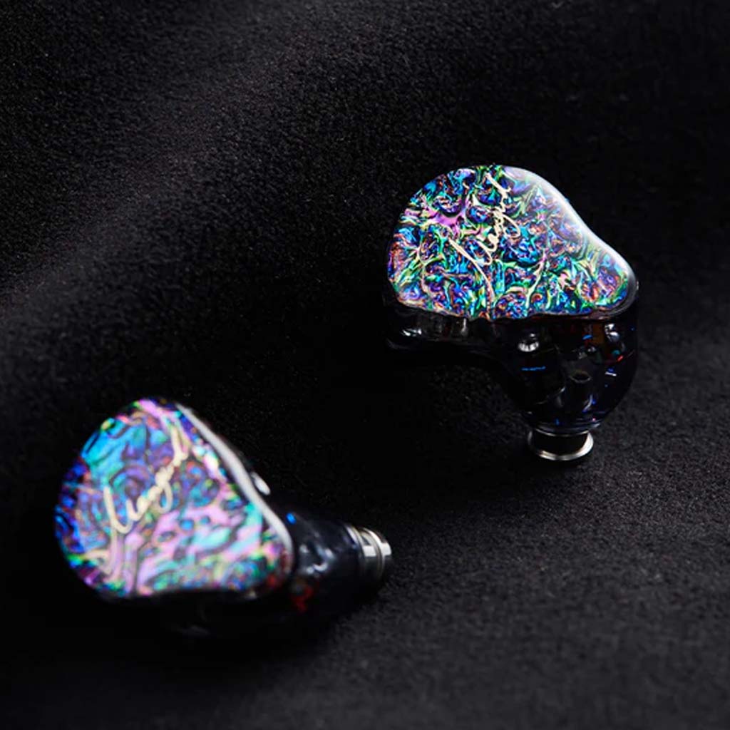 Pair of Mangird Top Pro IEMs with shimmering faceplates placed on black fabric, emphasizing luxury design and craftsmanship.